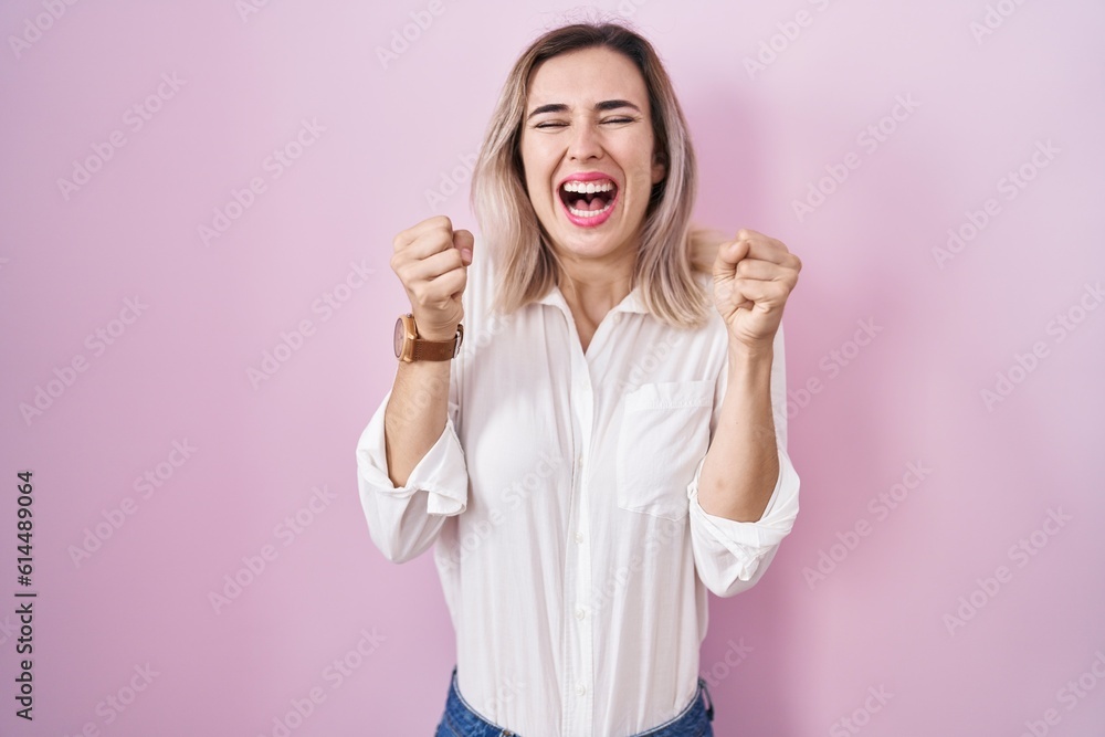 Young beautiful woman standing over pink background excited for success with arms raised and eyes closed celebrating victory smiling. winner concept. Young beautiful woman standing over pink background excited for success with arms raised and eyes closed celebrating victory smiling. winner concept.