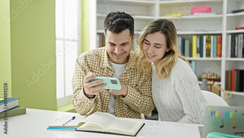 Man and woman students studying together using smartphone at library university