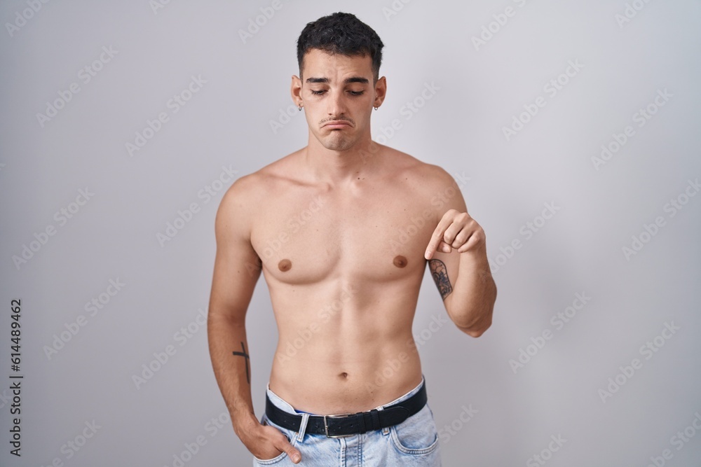 Handsome hispanic man standing shirtless pointing down looking sad and upset, indicating direction with fingers, unhappy and depressed. Handsome hispanic man standing shirtless pointing down looking sad and upset, indicating direction with fingers, unhappy and depressed.