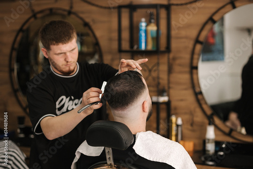 Back view of barber using sharp blade for shaving. Handsome customer sitting in barbershop