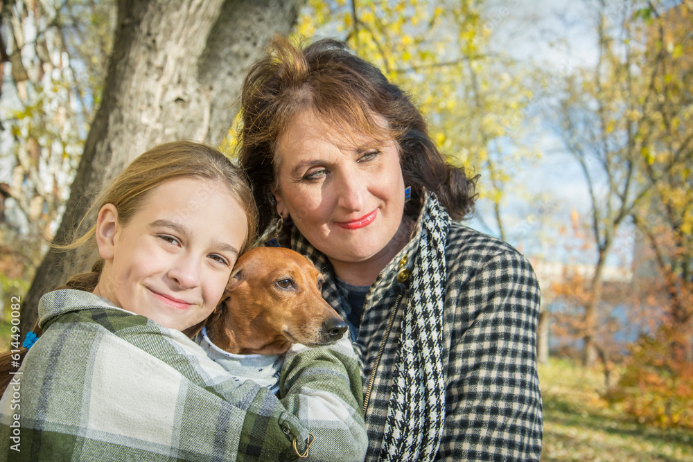 In the autumn park, a mother with her daughter holds a dachshund in her arms. In the autumn park, a mother with her daughter holds a dachshund in her arms.