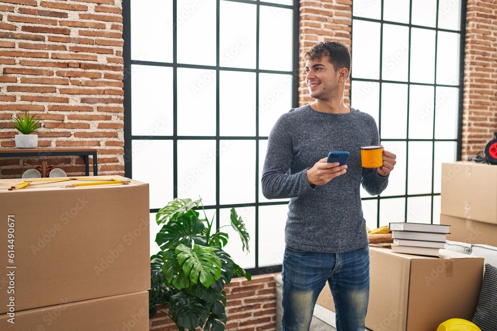Fotografie Young hispanic man using smartphone drinking coffee at new home