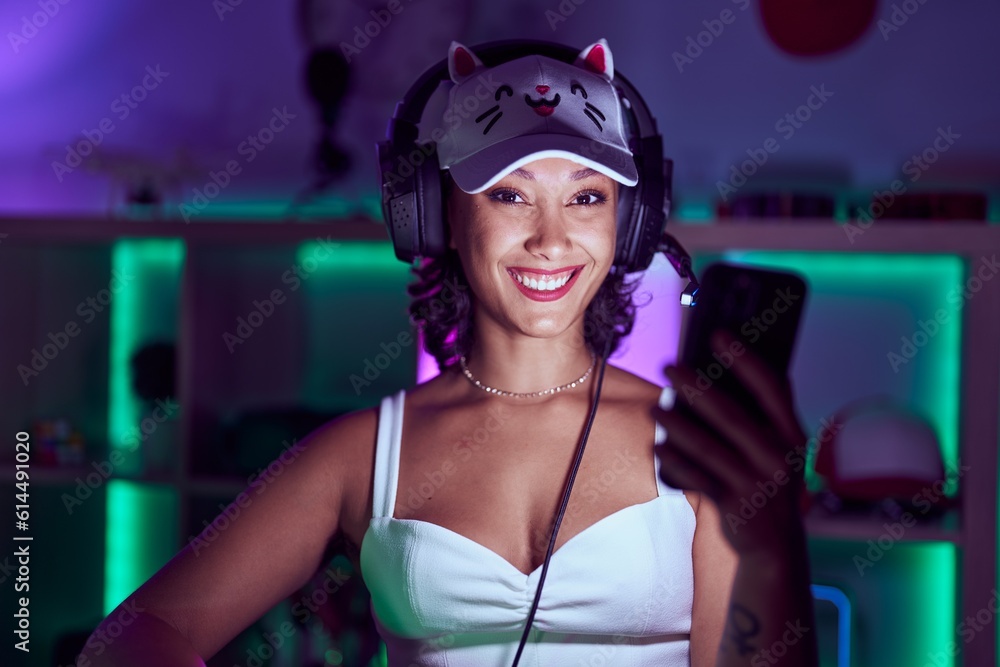 Young beautiful hispanic woman streamer smiling confident using smartphone at gaming room Young beautiful hispanic woman streamer smiling confident using smartphone at gaming room