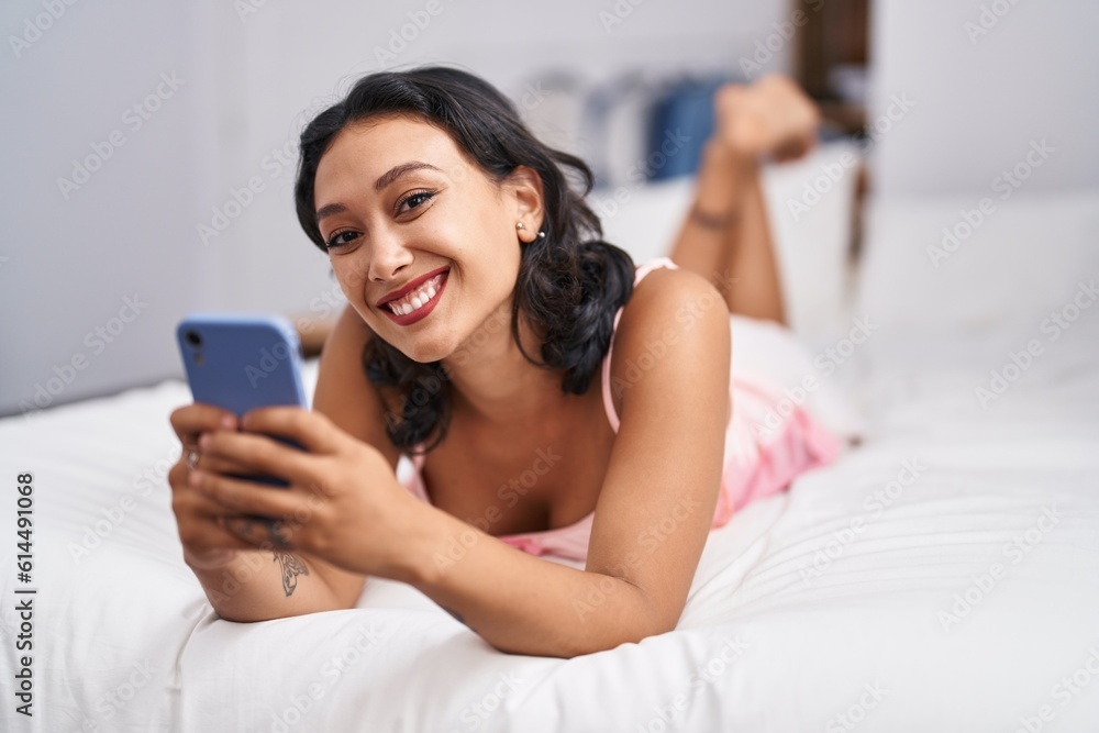 Young beautiful hispanic woman using smartphone lying on bed at bedroom Young beautiful hispanic woman using smartphone lying on bed at bedroom