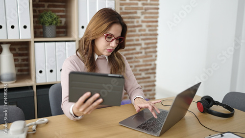 Young beautiful hispanic woman business worker using touchpad and laptop at office