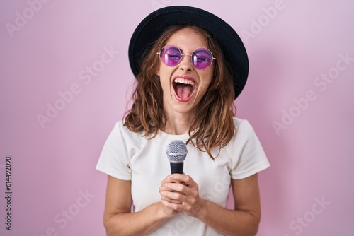 Beautiful brunette woman singing song using microphone smiling and laughing hard out loud because funny crazy joke.