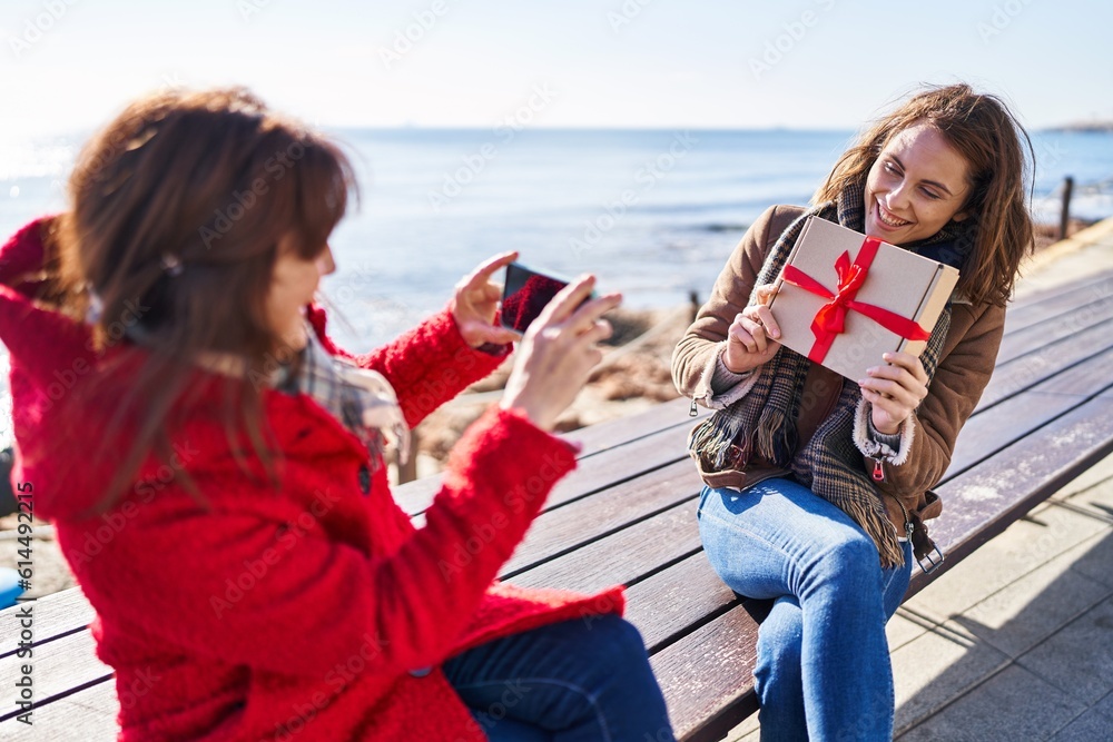 Two women mother and daughter make photo by smartphone holding gift at seaside