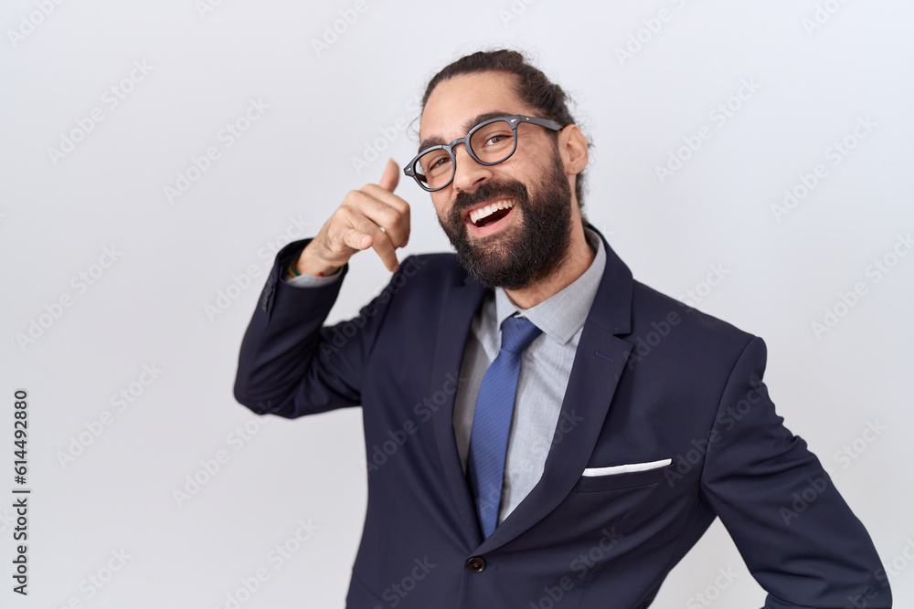 Hispanic man with beard wearing suit and tie smiling doing phone gesture with hand and fingers like talking on the telephone. communicating concepts. Hispanic man with beard wearing suit and tie smiling doing phone gesture with hand and fingers like talking on the telephone. communicating concepts.