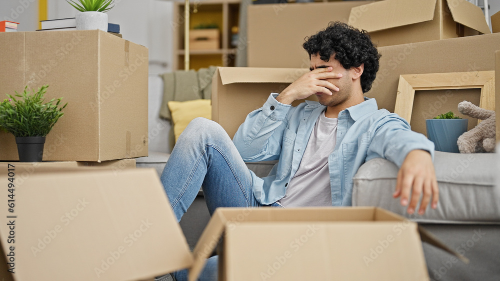 Young latin man sitting on floor stressed at new home Young latin man sitting on floor stressed at new home