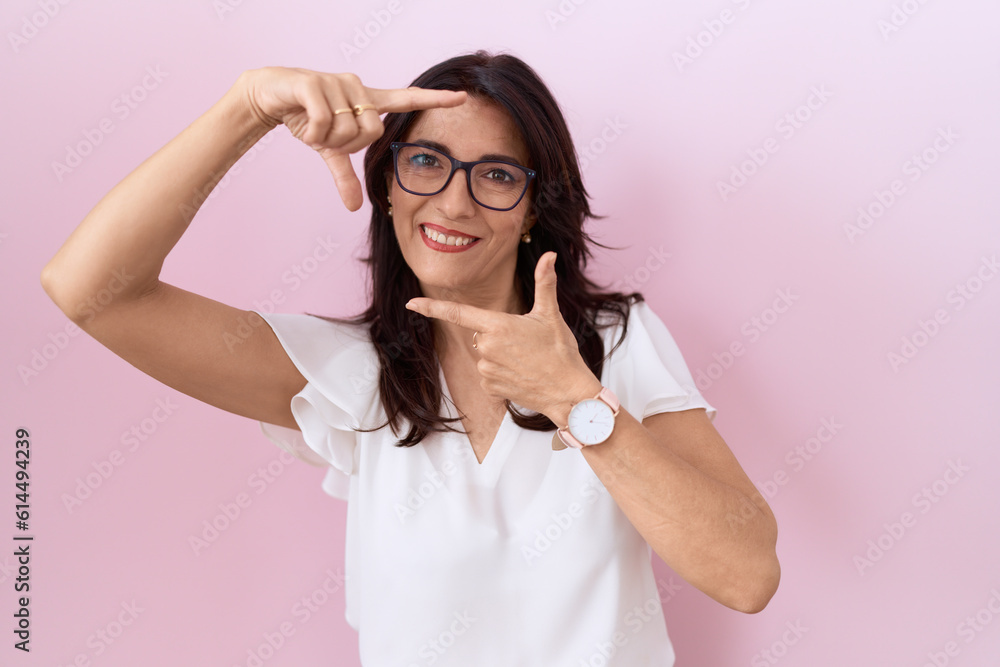 Middle age hispanic woman wearing casual white t shirt and glasses smiling making frame with hands and fingers with happy face. creativity and photography concept. Middle age hispanic woman wearing casual white t shirt and glasses smiling making frame with hands and fingers with happy face. creativity and photography concept.
