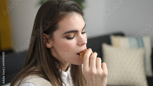 Young beautiful hispanic woman eating cookies sitting on the sofa at home