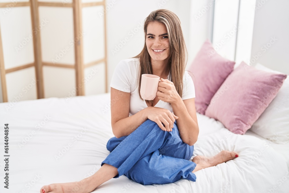 Young woman drinking cup of coffee sitting on bed at bedroom Young woman drinking cup of coffee sitting on bed at bedroom