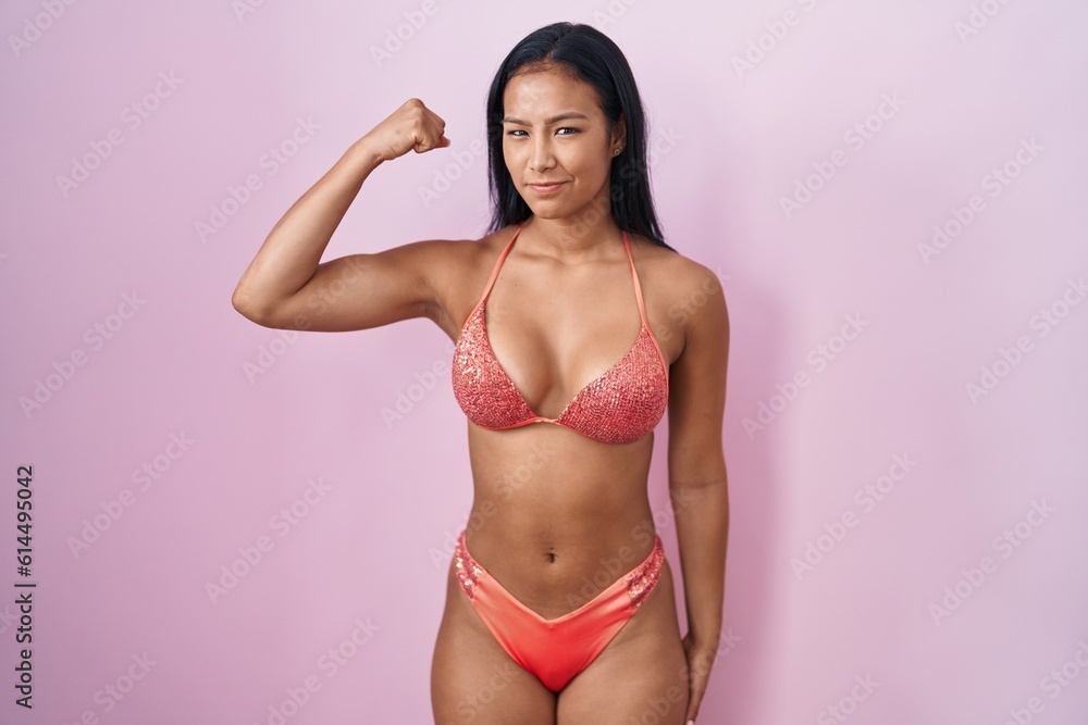 Hispanic woman wearing bikini strong person showing arm muscle, confident and proud of power Hispanic woman wearing bikini strong person showing arm muscle, confident and proud of power
