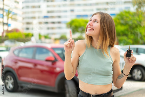 Young blonde woman holding car keys at outdoors intending to realizes the solution while lifting a finger up