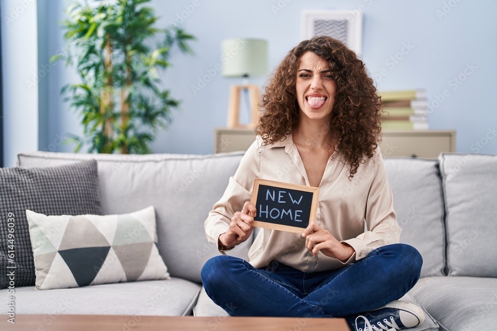 Hispanic woman with curly hair sitting on the sofa at new home sticking tongue out happy with funny expression. Hispanic woman with curly hair sitting on the sofa at new home sticking tongue out happy with funny expression.
