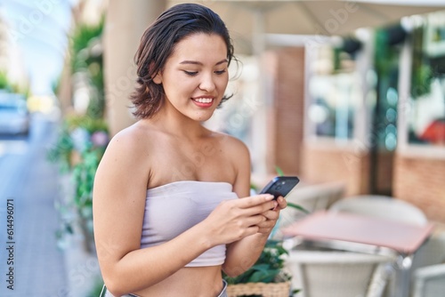 Young hispanic woman smiling confident using smartphone at coffee shop terrace