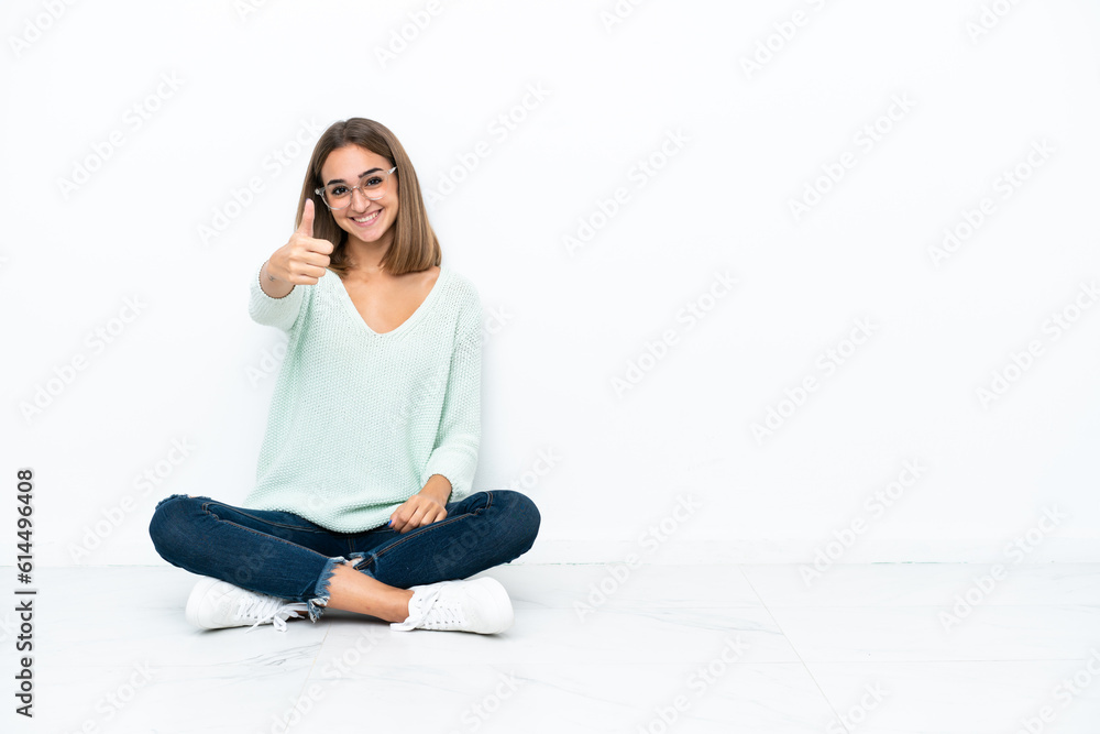 Young caucasian woman sitting on the floor isolated on white background with thumbs up because something good has happened Young caucasian woman sitting on the floor isolated on white background with thumbs up because something good has happened