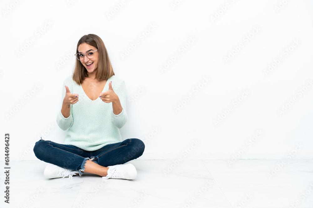Young caucasian woman sitting on the floor isolated on white background pointing to the front and smiling Young caucasian woman sitting on the floor isolated on white background pointing to the front and smiling