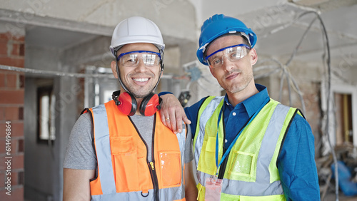 Two men builders smiling confident standing together at construction site