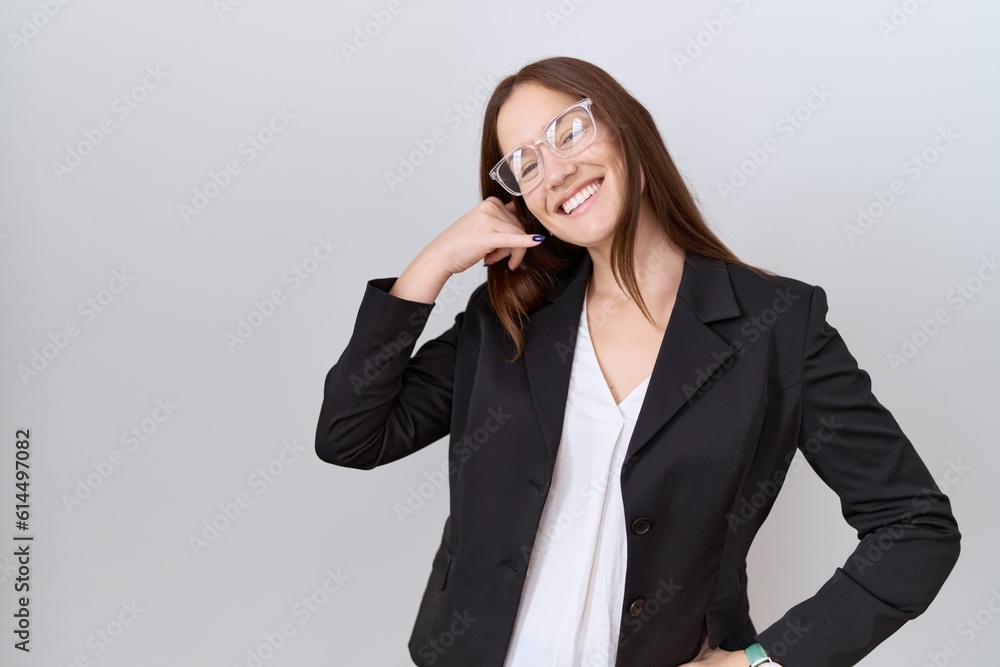 Beautiful brunette woman wearing business jacket and glasses smiling doing phone gesture with hand and fingers like talking on the telephone. communicating concepts. Beautiful brunette woman wearing business jacket and glasses smiling doing phone gesture with hand and fingers like talking on the telephone. communicating concepts.