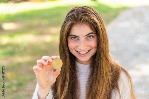 Young pretty caucasian woman holding a Bitcoin at outdoors with happy expression