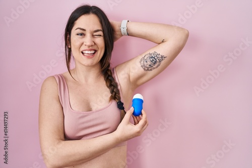 Young brunette woman using roll on deodorant winking looking at the camera with sexy expression, cheerful and happy face.