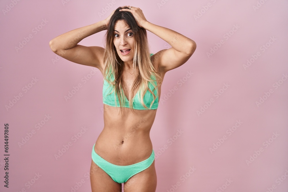 Fototapeta premium Young hispanic woman wearing bikini over pink background crazy and scared with hands on head, afraid and surprised of shock with open mouth