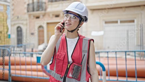 Young beautiful hispanic woman builder smiling confident talking on smartphone at street