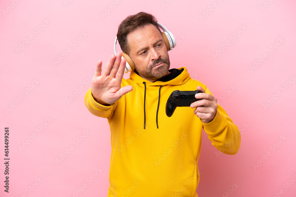 Middle age man playing with a video game controller isolated on pink background making stop gesture and disappointed Middle age man playing with a video game controller isolated on pink background making stop gesture and disappointed
