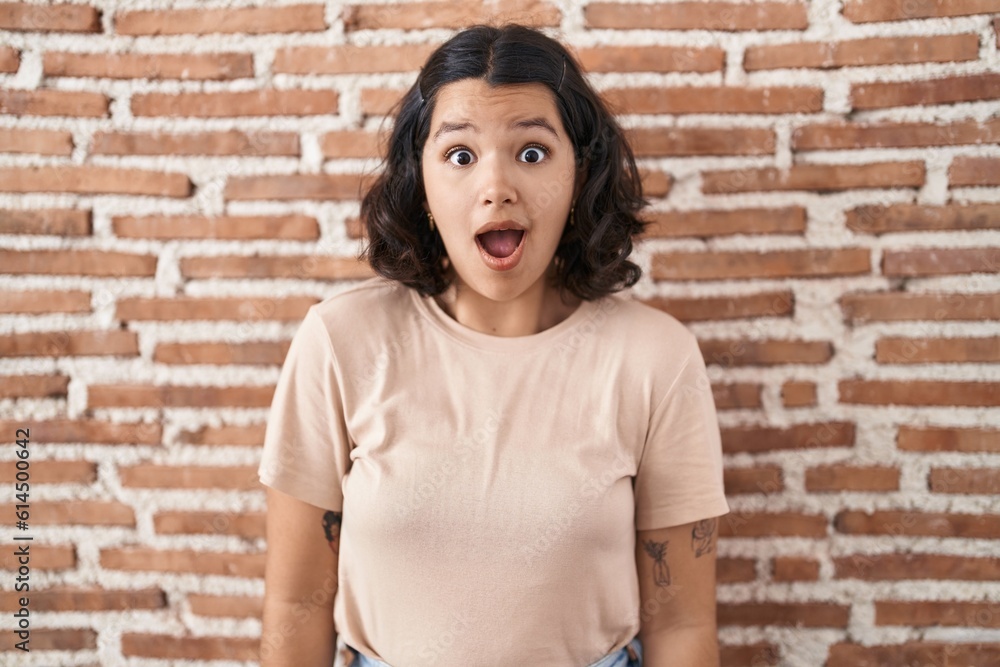 Young hispanic woman standing over bricks wall afraid and shocked with surprise and amazed expression, fear and excited face. Young hispanic woman standing over bricks wall afraid and shocked with surprise and amazed expression, fear and excited face.