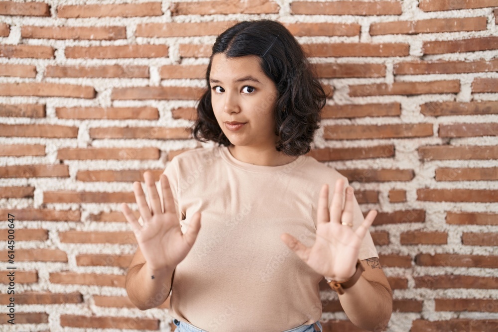 Young hispanic woman standing over bricks wall moving away hands palms showing refusal and denial with afraid and disgusting expression. stop and forbidden. Young hispanic woman standing over bricks wall moving away hands palms showing refusal and denial with afraid and disgusting expression. stop and forbidden.