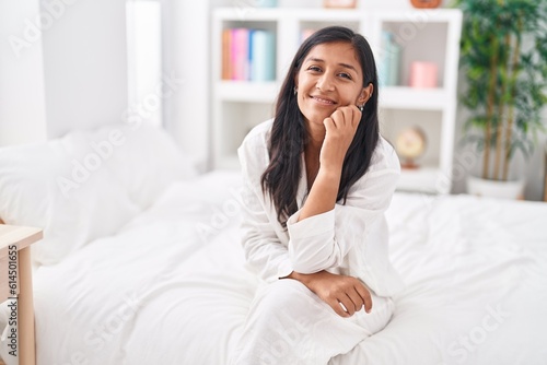 Young beautiful hispanic woman smiling confident sitting on bed at bedroom