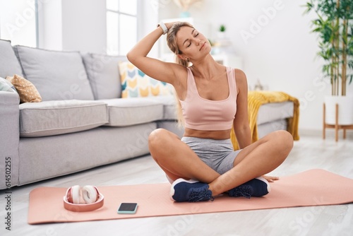 Young blonde woman stretching head sitting on floor at home