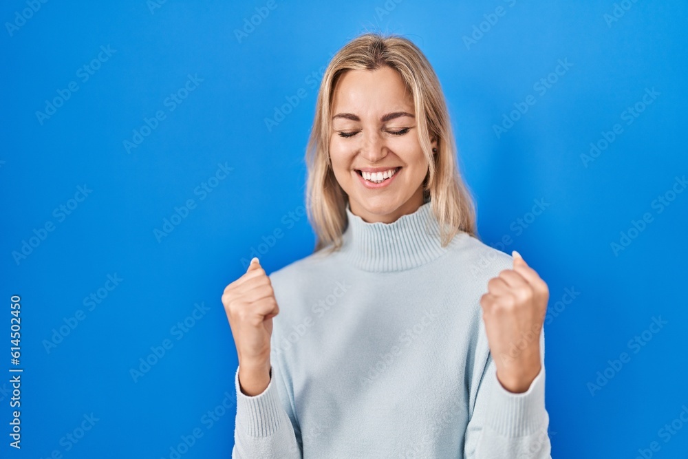 Young caucasian woman standing over blue background very happy and excited doing winner gesture with arms raised, smiling and screaming for success. celebration concept. Young caucasian woman standing over blue background very happy and excited doing winner gesture with arms raised, smiling and screaming for success. celebration concept.