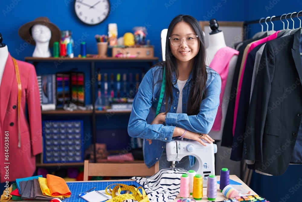 Fototapeta premium Young chinese woman tailor smiling confident leaning on sewing machine at clothing factory