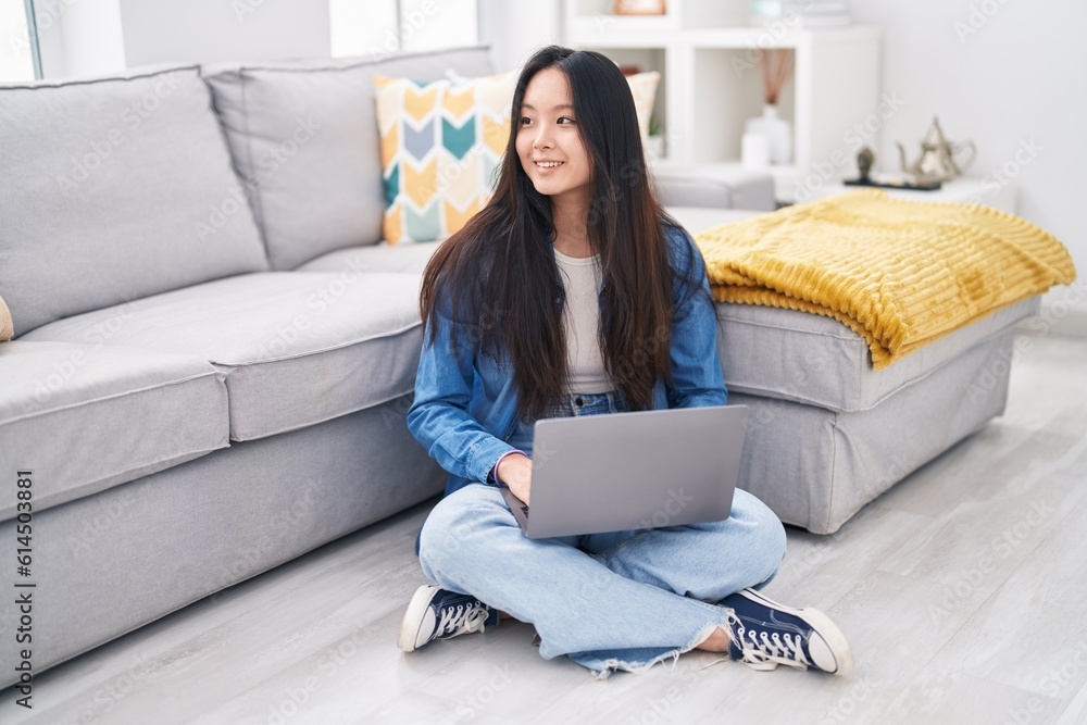 Young chinese woman using laptop sitting on floor at home