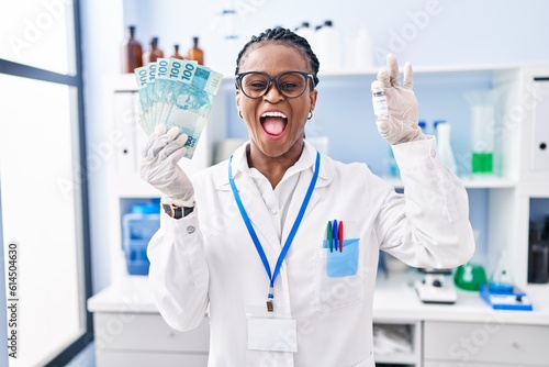 African woman with braids working at scientist laboratory holding money celebrating crazy and amazed for success with open eyes screaming excited.