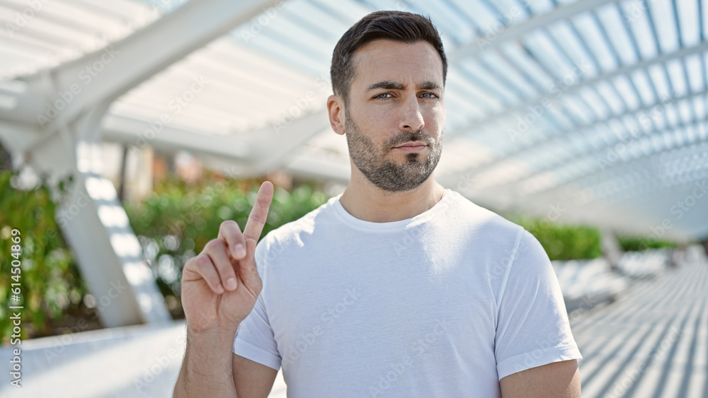 Young hispanic man standing with serious expression saying no with finger at park Young hispanic man standing with serious expression saying no with finger at park