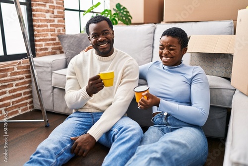 Man and woman couple drinking coffee sitting on floor at new home