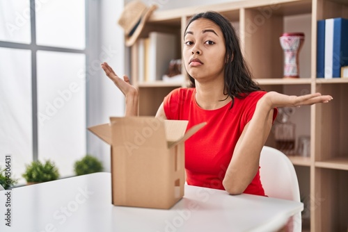 Young brazilian woman looking inside cardboard box shouting and screaming loud to side with hand on mouth. communication concept.