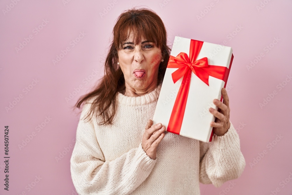 Middle age hispanic woman holding present sticking tongue out happy with funny expression. Middle age hispanic woman holding present sticking tongue out happy with funny expression.