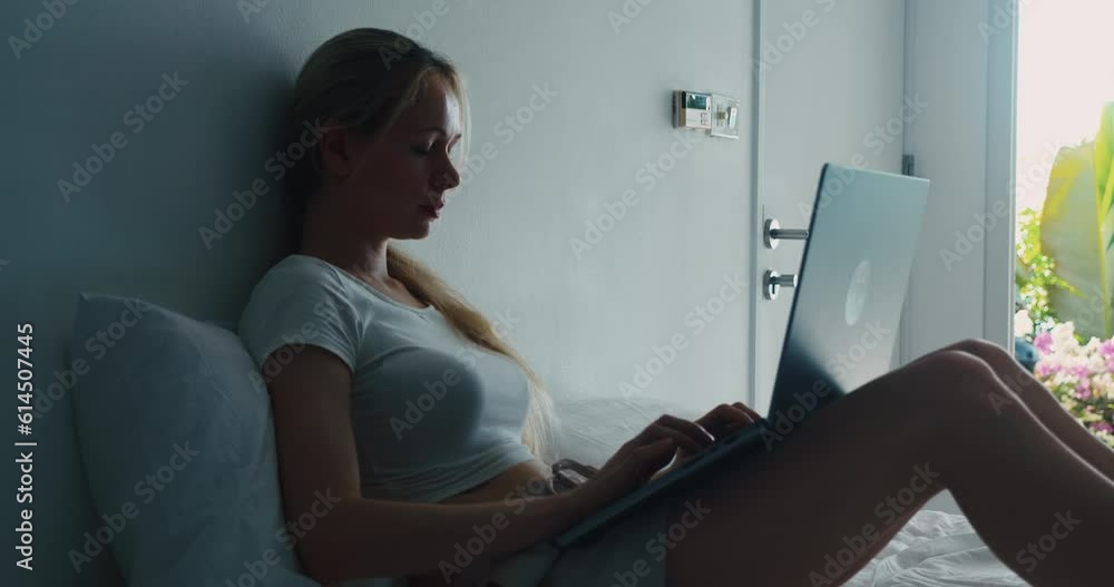 Silhouette young female 30 years old use laptop computer lying at home on the bed in her bedroom. A young female student uses a computer on a day off at home in the bedroom Silhouette young female 30 years old use laptop computer lying at home on the bed in her bedroom. A young female student uses a computer on a day off at home in the bedroom