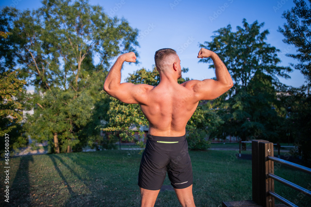 A bodybuilder shows off his back muscles and biceps during a workout in an open-air park A bodybuilder shows off his back muscles and biceps during a workout in an open-air park