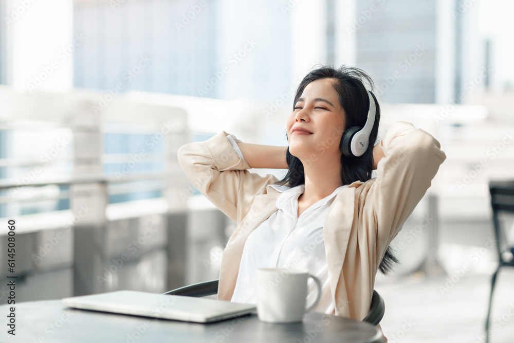 Happy young adult business woman freelancer listening music with headphones while working with laptop at outdoor co-working space, remote work and work anywhere concept...