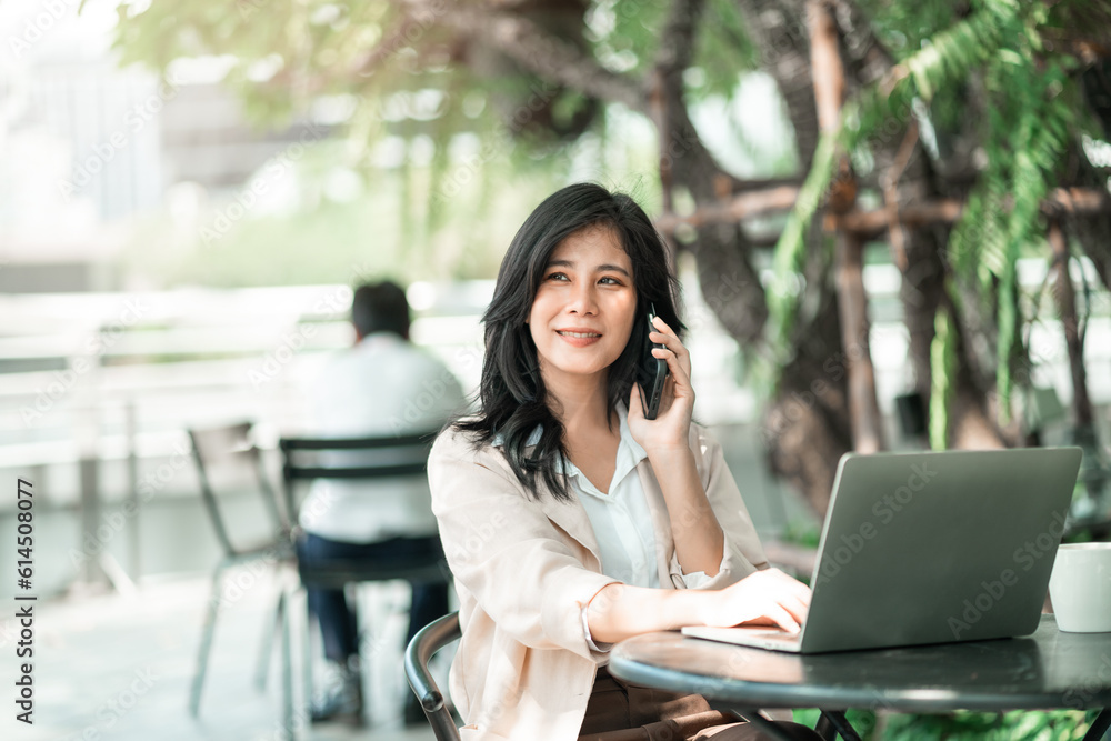 Attractive asian business woman using smartphone for talking with colleague while using laptop for work at co-working space, Urban business people, work anywhere lifestyles. Attractive asian business woman using smartphone for talking with colleague while using laptop for work at co-working space, Urban business people, work anywhere lifestyles.