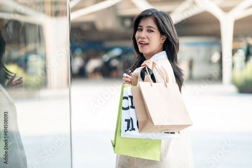 Cheerful asian business woman shopaholic girl carrying shopping bag while walking in shopping mall. Lifestyle of people on weekend.