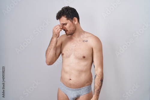 Young hispanic man standing shirtless wearing underware tired rubbing nose and eyes feeling fatigue and headache. stress and frustration concept.