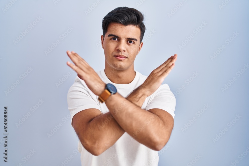 Hispanic man standing over blue background rejection expression crossing arms doing negative sign, angry face Hispanic man standing over blue background rejection expression crossing arms doing negative sign, angry face