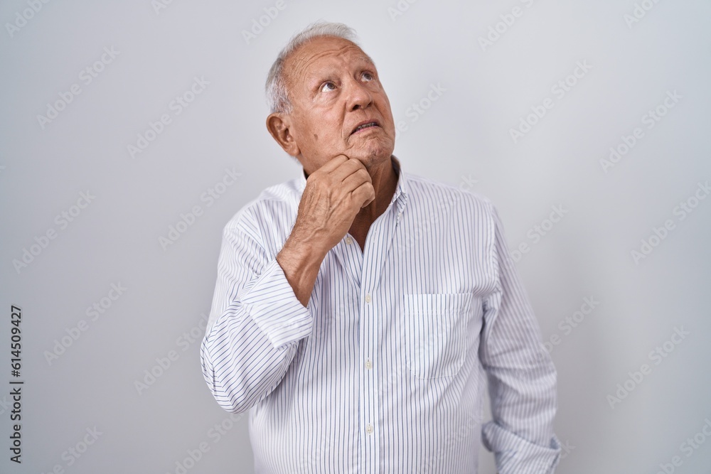 Senior man with grey hair standing over isolated background with hand on chin thinking about question, pensive expression. smiling with thoughtful face. doubt concept. Senior man with grey hair standing over isolated background with hand on chin thinking about question, pensive expression. smiling with thoughtful face. doubt concept.