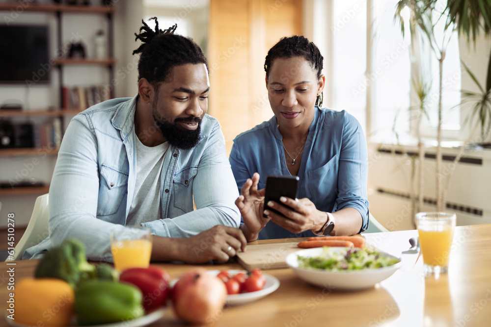 Happy African American couple using a phone while having breakfast in the morning.Focus is on woman